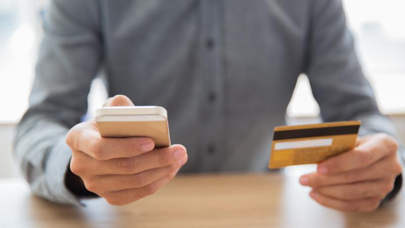 un uomo effettua un pagamento online riportando sul cellulare il numero della carta di credito